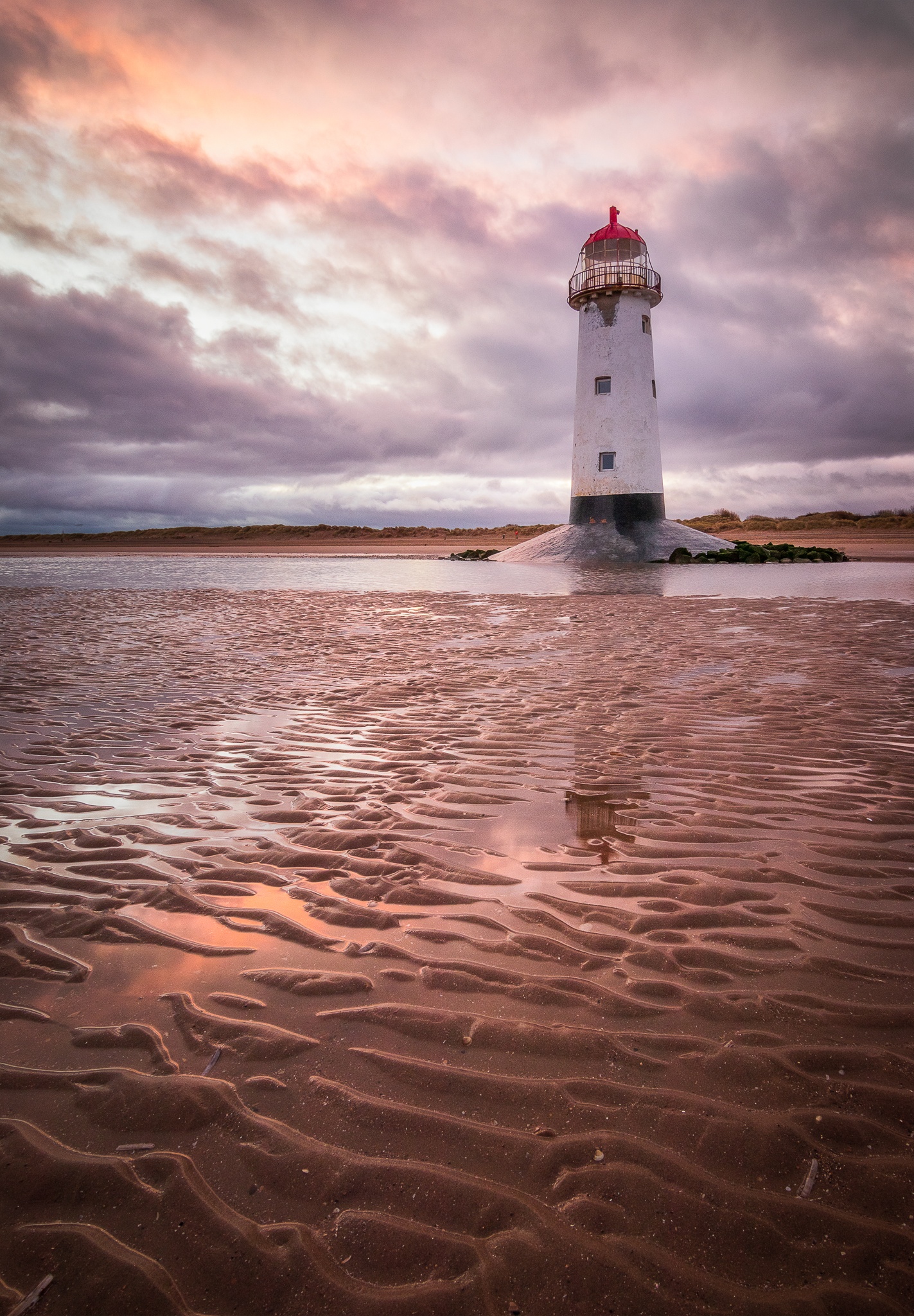 Talacre Lighthouse at dawn under a glowing cloudy sky and reflected in pools at low tide. Prints available for purchase.